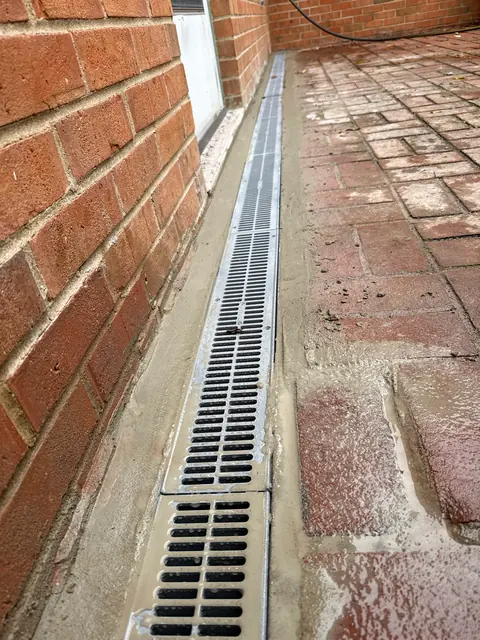 New channel drain set in concrete along the foundation of a brick building.